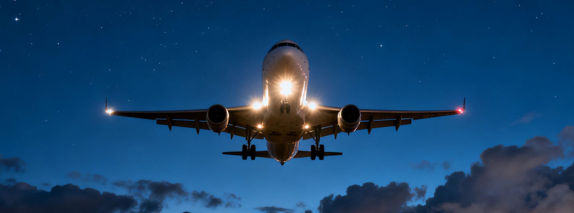 Commercial aircraft on approach with landing lights illuminated against starry night sky